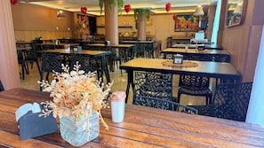 Interior de un restaurante con mesas y sillas de madera, un jarrón con flores secas y un atril para el menú.