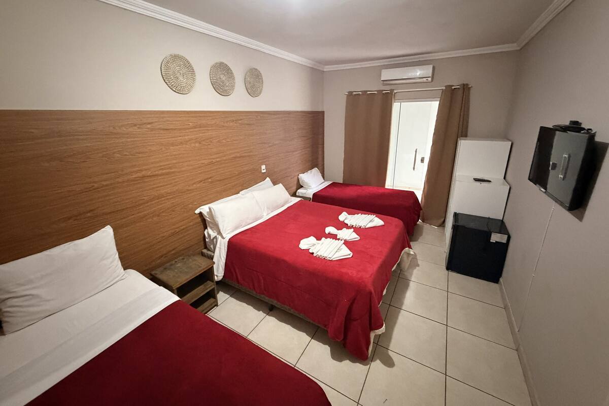 Habitación de hotel con dos camas, cabecero de madera, televisor de pantalla plana, minibar y una puerta con cortinas.