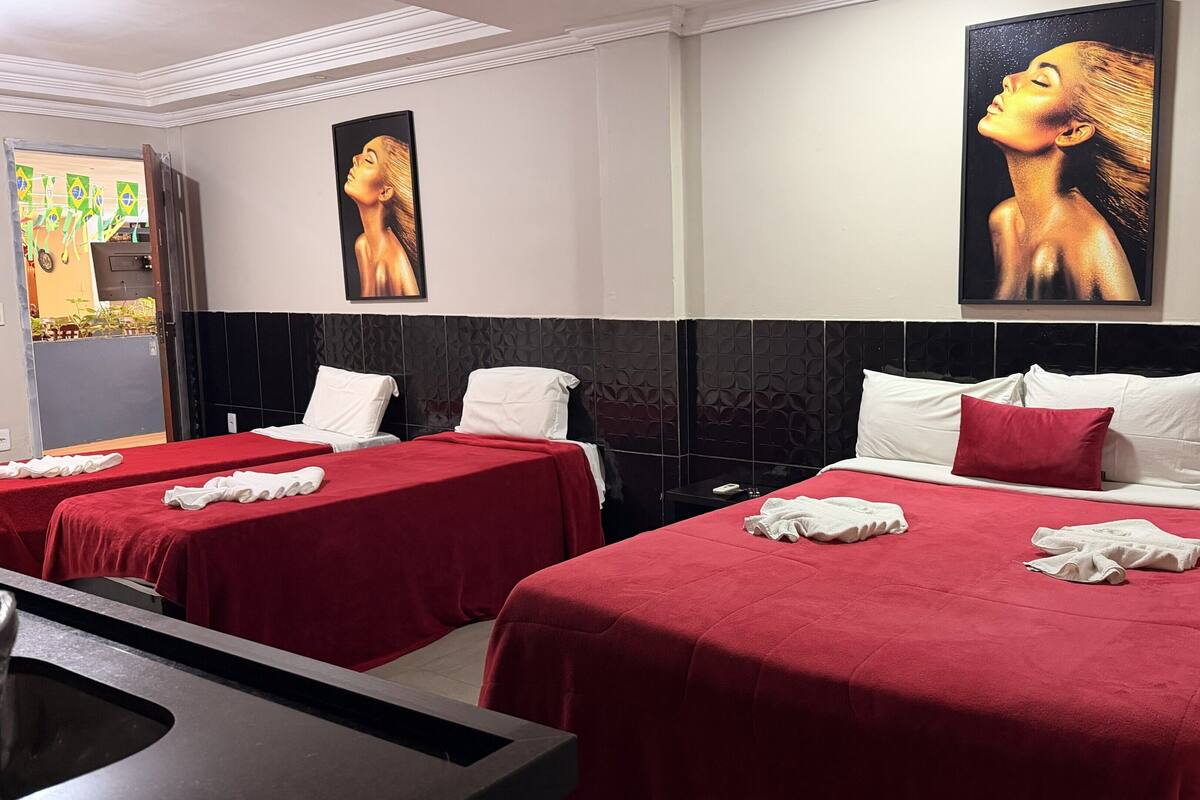 Habitación de hotel con dos camas, cubrecamas rojos, almohadas blancas y obras de arte en las paredes.