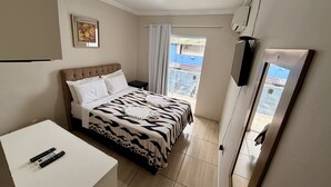 Un dormitorio con cama, escritorio, televisor y ventana con cortinas.