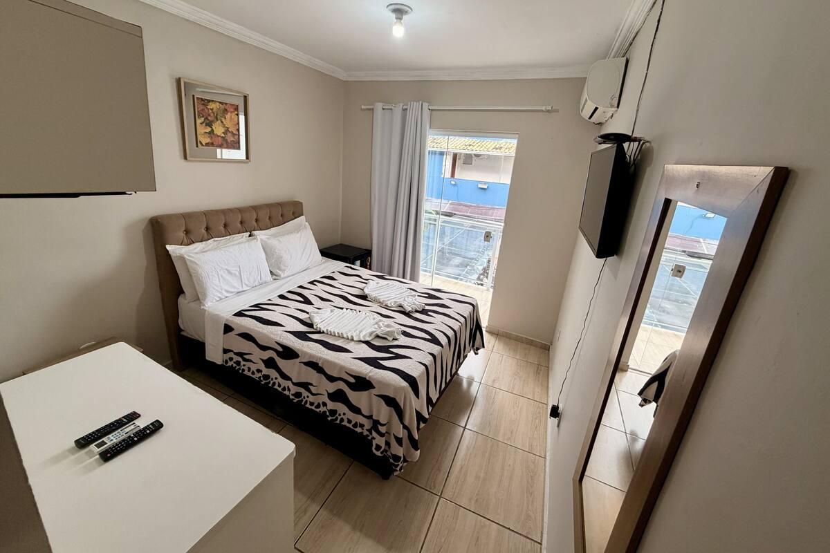 Un dormitorio con cama, escritorio, televisor y ventana con cortinas.