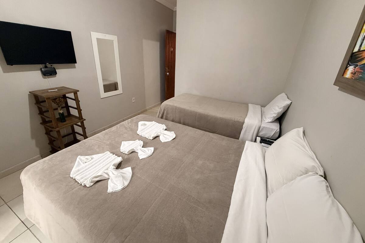 Un dormitorio con una cama, un televisor montado en la pared, una mesita de noche de madera y un espejo.
