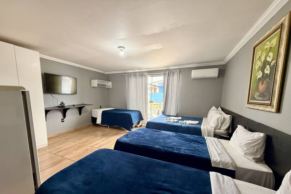Habitación de hotel con dos camas, un televisor, un televisor de pantalla plana montado en la pared, un equipo de aire acondicionado y un cuadro en la pared.