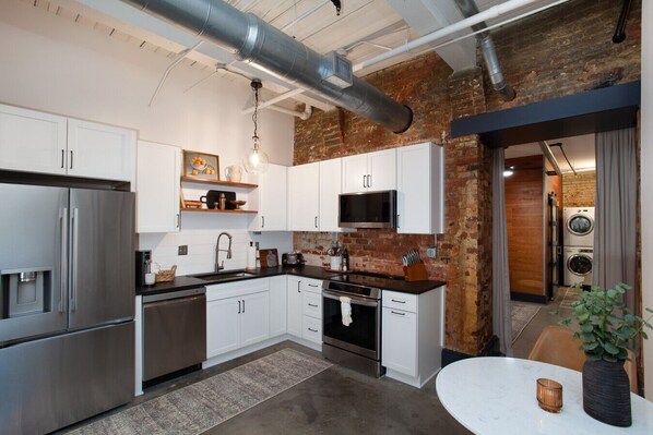 A modern kitchen with stainless steel appliances, white cabinetry, and a brick accent wall. - Stylish Loft on South Gay | Downtown Knoxville (Knoxville)