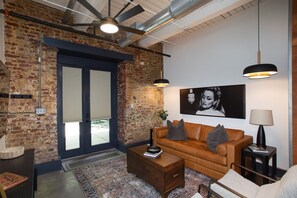 A modern living room with a brick wall, a brown leather sofa, a coffee table, and a ceiling fan. - Stylish Loft on South Gay | Downtown Knoxville (Knoxville)