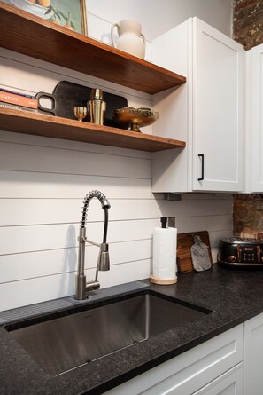 A kitchen with a black sink, wooden shelves, and white cabinets. - Stylish Loft on South Gay | Downtown Knoxville (Knoxville)