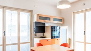 Ett kompakt kök med ett matbord och stolar, en inbyggd ugn och en tv.