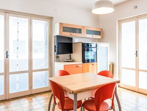 A compact kitchen with a dining table and chairs, a built-in oven, and a television. - La Caracola by Interhome (Marina di Andora)