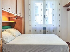 A bedroom with a bed, a bedside table, a lamp, and a window with curtains. - La Caracola by Interhome (Marina di Andora)