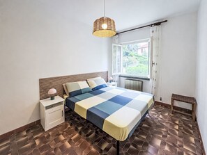 Ein Schlafzimmer mit Bett, Nachttisch, Lampe und einem Fenster mit Vorhängen.