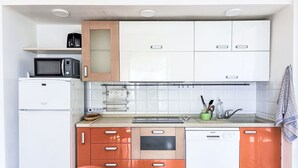 Ett kompakt kök med vita och orange skåp, en mikrovågsugn, en brödrost och en diskmaskin.