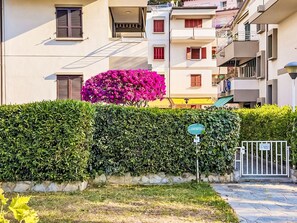 Ein Wohngebäude mit geschlossenem Eingang, einer Hecke und einem üppigen, rosa blühenden Strauch.