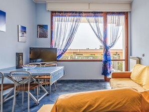Ein Zimmer mit einem Bett, einem Fernseher, einem Tisch mit Stühlen und einem Fenster mit Vorhängen.