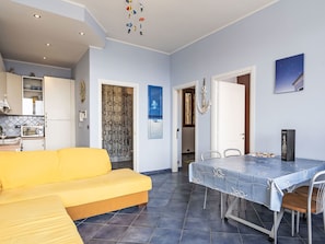 Ein Wohnzimmer mit einem gelben Sofa, einem Esstisch mit blauer Tischdecke und einer Küchenzeile mit einer Mikrowelle.