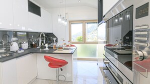 Cocina moderna con una isla grande, electrodomésticos de acero inoxidable y un taburete rojo.