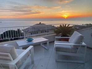 A balcony with white furniture, a potted plant, and a view of the sea at sunset. - Wonderful Sea View Apartment (Genova)