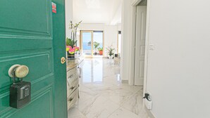 Un pasillo con una puerta verde, suelo de mármol y vistas al exterior.