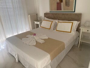 A neatly made bed with a beige bedspread and white pillows, a white nightstand with a lamp, and a framed picture on the wall. - Wonderful Sea View Apartment (Genova)