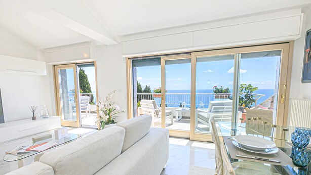 Un salón moderno con sofá, una mesa de centro de vidrio y un balcón con vista al mar.