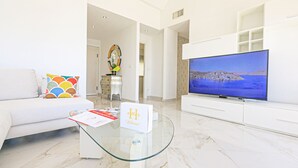 Una sala de estar moderna con un sofá, una mesa de centro de vidrio, un televisor de pantalla plana y un espejo decorativo.