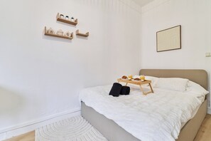 Quarto com cama, mesa de cabeceira com bandeja de itens para o café da manhã e duas prateleiras de madeira na parede.