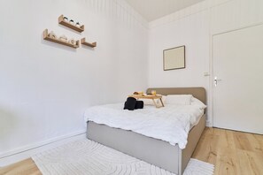 Quarto minimalista com uma cama, mesa de cabeceira, prateleira na parede e uma porta.