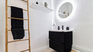 Un baño con tocador blanco, armarios negros, un espejo redondo, una escalera de madera y un taburete pequeño.
