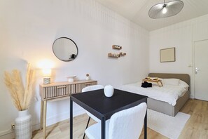 Quarto com cama, mesa de cabeceira, espelho e uma pequena escrivaninha com cadeira.