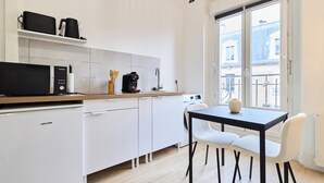 Una cocina moderna con armarios blancos, microondas, cafetera y comedor con mesa y sillas.