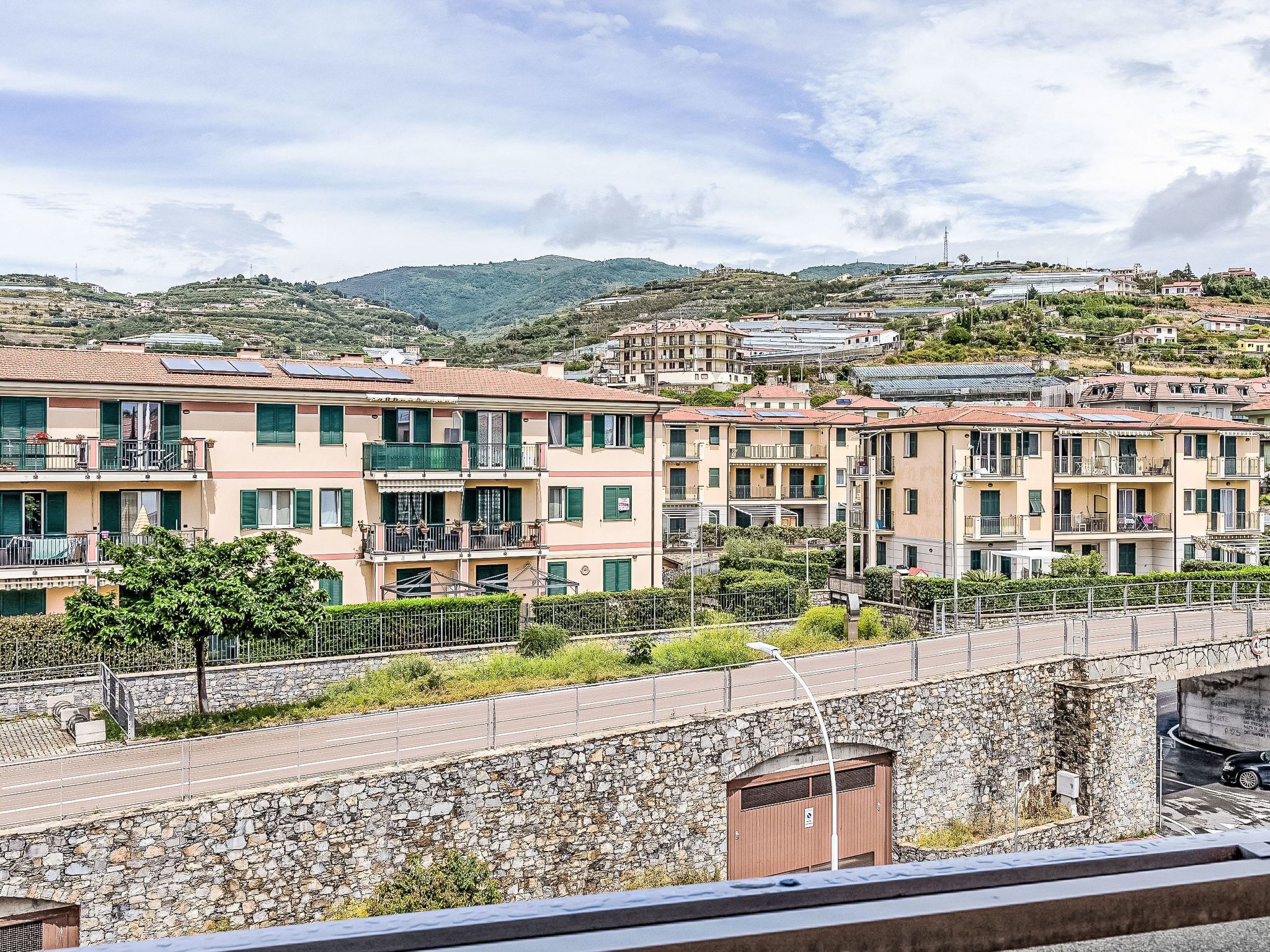 A residential area with multi-story buildings, a stone wall, and a road.