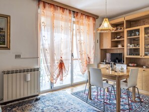 A dining area with a table, chairs, a hanging light fixture, a radiator, and a large window with sheer curtains. - Casa di Flavia by Interhome (Riva Ligure)