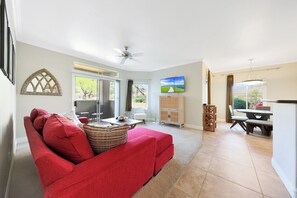 Ein Wohnzimmer mit einem roten Sofa, einem Deckenventilator, einem Fernseher und einem Essbereich mit Tisch und Stühlen.