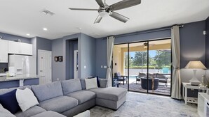Uma sala de estar moderna com sofá seccional, ventilador de teto e vista para um pátio externo.