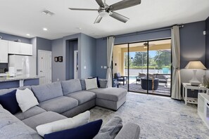 Ein modernes Wohnzimmer mit einem Ecksofa, Deckenventilator und Blick auf eine Terrassenanlage.