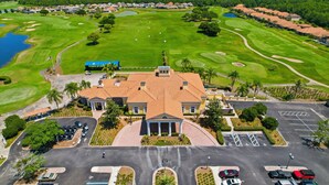 Um campo de golfe com um clube, parque de estacionamento e vegetação ao redor.