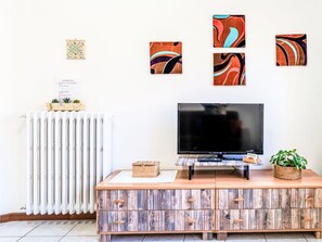 Een woonkamer met een televisie, een houten kast, een radiator en abstracte decoratie aan de muur.