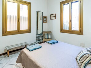 Ein Schlafzimmer mit einem Bett, einer Bank, einem Spiegel und zwei Fenstern mit Jalousien.