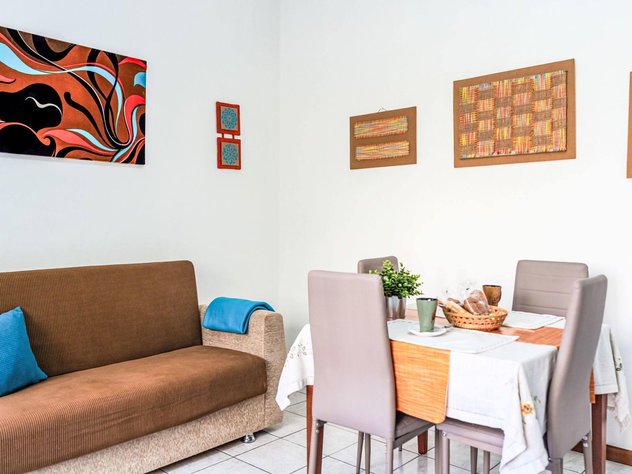 Un salon avec un canapé marron, une table à manger avec des chaises et des œuvres d’art accrochées au mur.