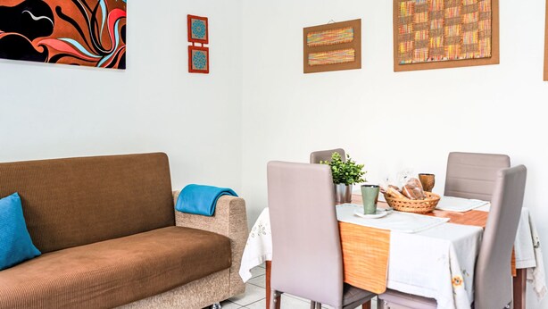 Ein Wohnzimmer mit einem braunen Sofa, einem Esstisch mit Stühlen und Wandbildern.