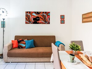 Een moderne woonkamer met een bruine bank, kleurrijke kussens, een eettafel met een plant en abstracte wanddecoratie.