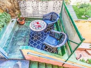 Een terras met een mozaiektafel, twee blauwe stoelen, een potplant en een klein zwembad.