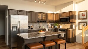 A modern kitchen with a stainless steel refrigerator, granite countertops, and wooden cabinets. - Modern 1BR Penthouse  Heart of CLE Views (Cleveland)
