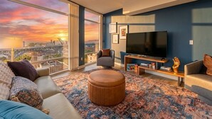 A modern living room with a large TV, comfortable seating, a view of the city, and a large window. - Modern 1BR Penthouse  Heart of CLE Views (Cleveland)