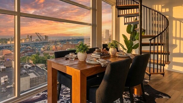 A dining area with a view of a cityscape and a spiral staircase. - Modern 1BR Penthouse  Heart of CLE Views (Cleveland)