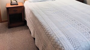 Ein ordentlich bezogenes Bett mit einer gemusterten Tagesdecke, einer Nachttischlampe und einem Nachttisch mit einer Schublade.