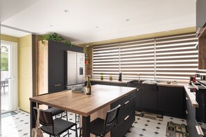 A modern kitchen with a wooden island, black cabinets, and a large window with blinds. - La Brise - À moins d’1 km de la plage (Fréhel)