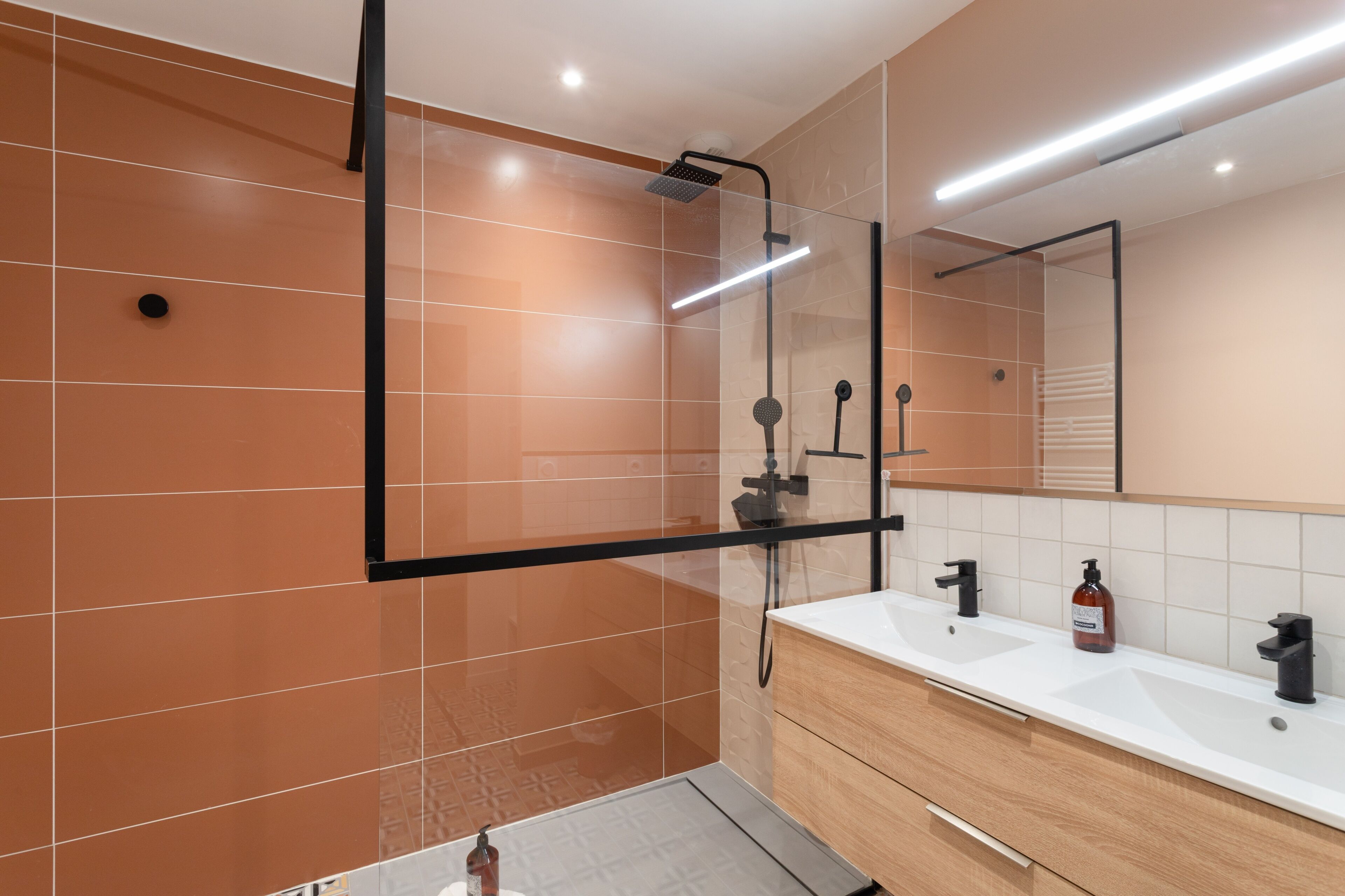 A modern bathroom with a glass-enclosed shower, a white sink with a wooden vanity, and a large mirror above the vanity.