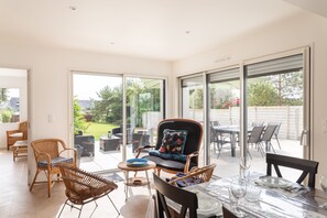 A spacious patio with wicker furniture, a dining table set for two, and a large sliding glass door leading to a garden. - La Brise - À moins d’1 km de la plage (Fréhel)