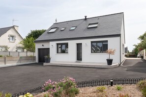 Una moderna casa a due piani con tetto spiovente, ampie finestre e una recinzione in metallo nero in primo piano.