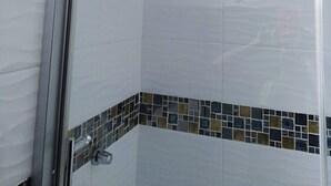 Ducha con puerta de vidrio, ventana pequeña y suelo de baldosas con un borde decorativo.